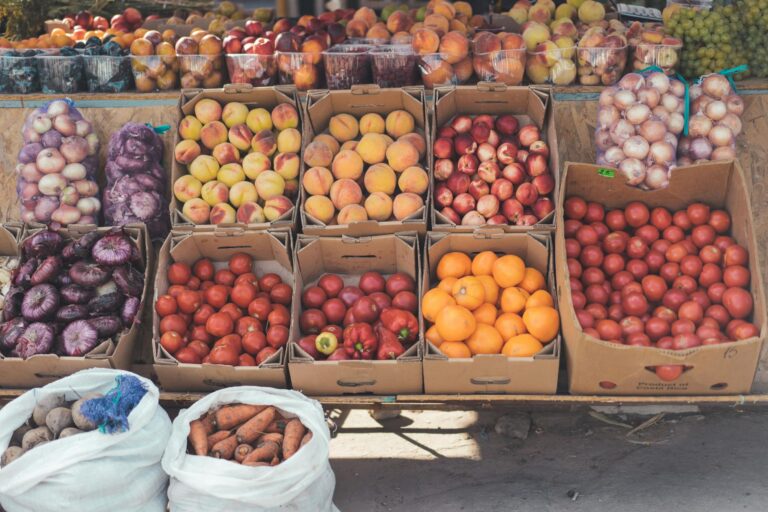 Colorful fruits and vegetables arranged in boxes at an outdoor market stall.