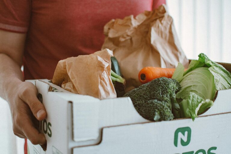Person holding a box filled with fresh vegetables, ideal for health and produce concepts.